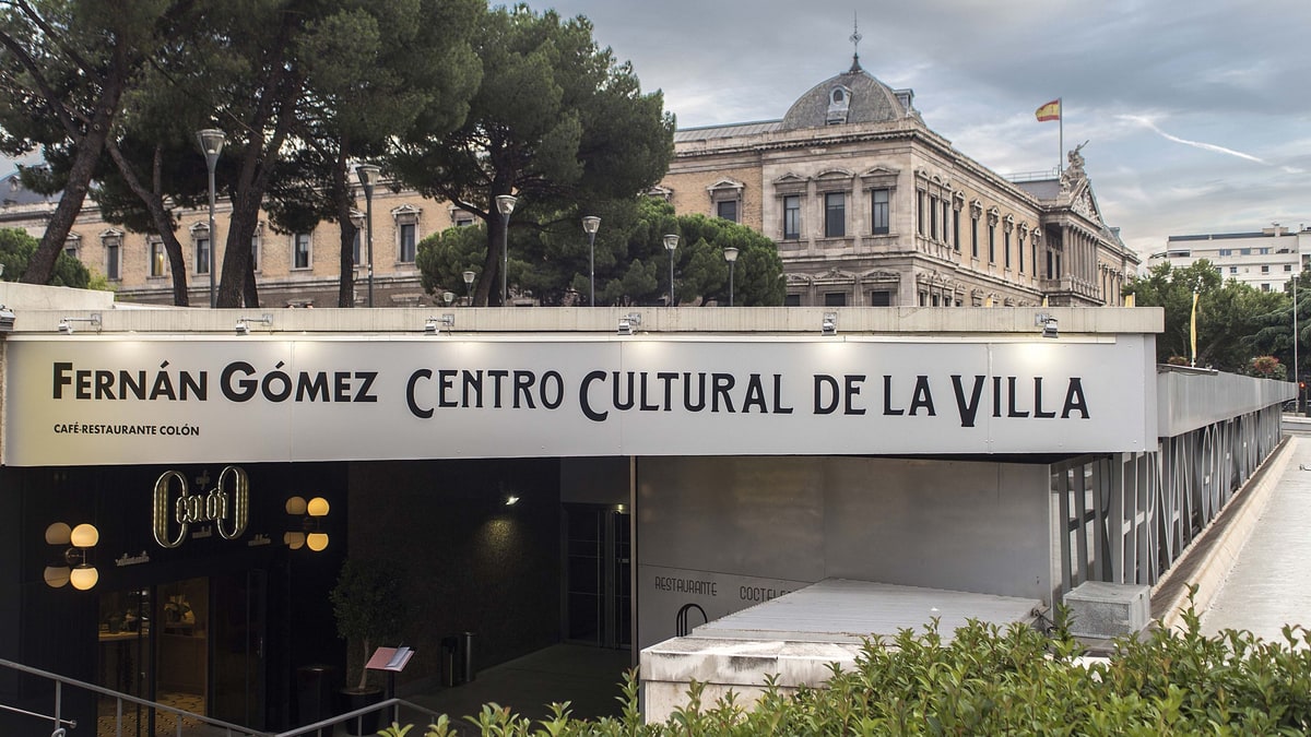 Entrada del Fernán Gómez Centro Cultural de la Villa con la Biblioteca Nacional al fondo, bajo cielo nublado.