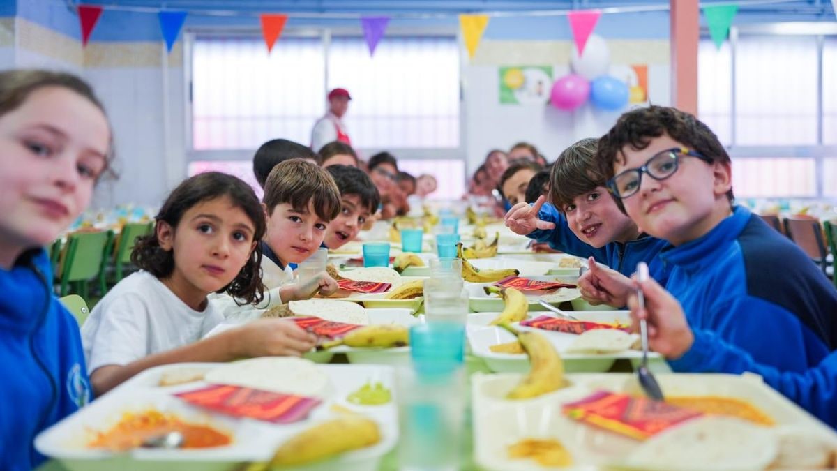 Imagen ilustrativa: una mesa de comedor escolar con bandejas vacías y servilletas dobladas bajo un cielo azul