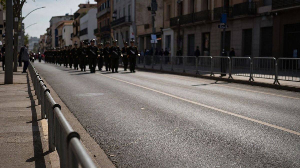 Imagen ilustrativa: una avenida urbana preparada para un desfile militar, con vallas metálicas y luz de mañana