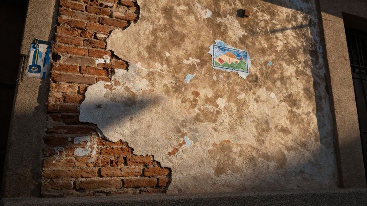 Imagen ilustrativa: detalle de una pared de ladrillo y yeso envejecida, con restos de pintura desgastada al atardecer