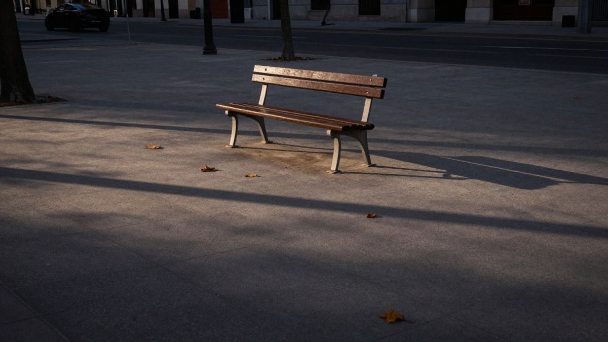 Imagen ilustrativa: un banco de madera vacío en un bulevar urbano al atardecer, con hojas caídas en el suelo
