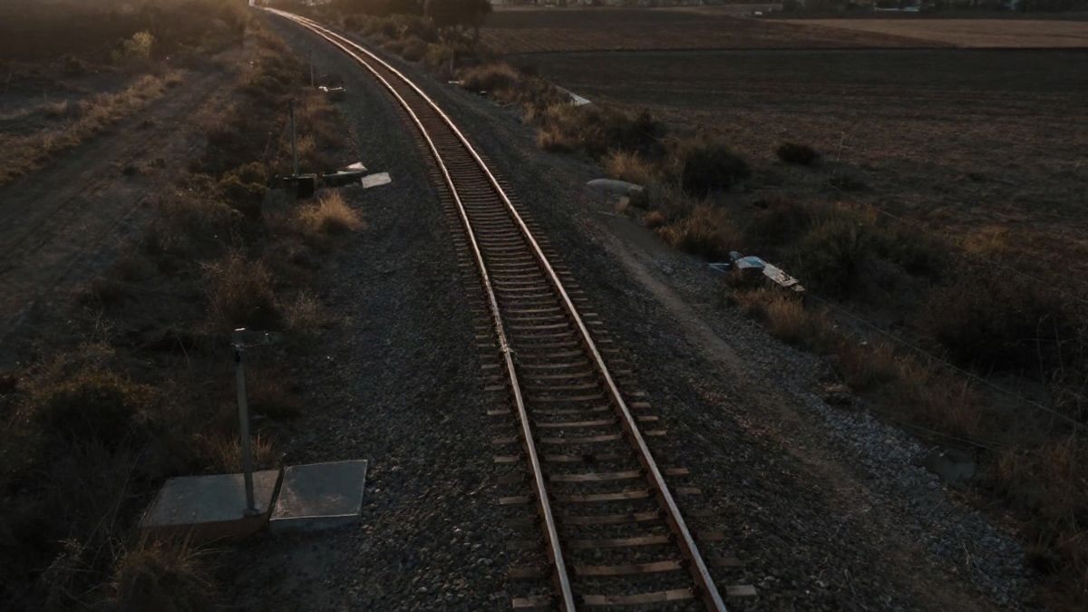 Imagen ilustrativa: vía de tren vista desde arriba al atardecer, con sombras largas sobre un paisaje llano