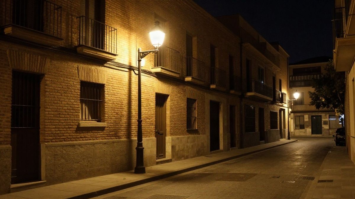 Imagen ilustrativa: calle residencial de noche con una farola encendida y sombras alargadas sobre la acera