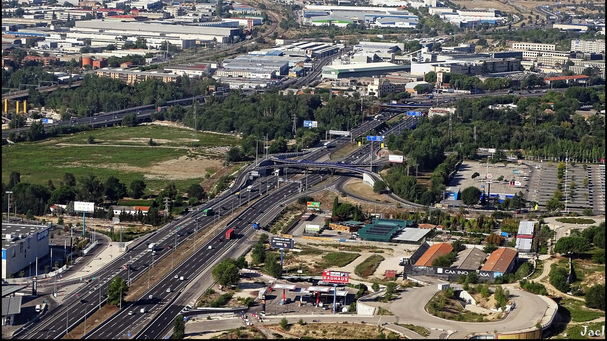 Vista aérea de enlaces de autovía en Madrid con tráfico circulando y polígonos industriales al fondo.