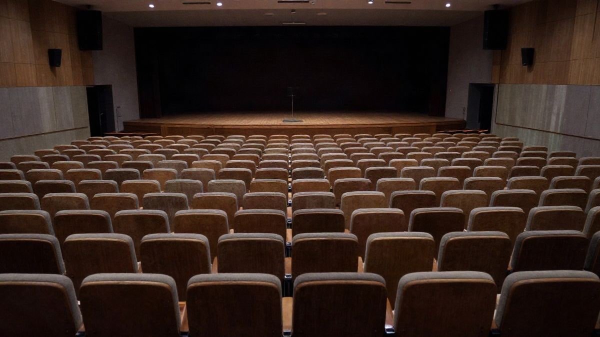 Imagen ilustrativa: un auditorio vacío con filas de butacas que convergen hacia un escenario en penumbra