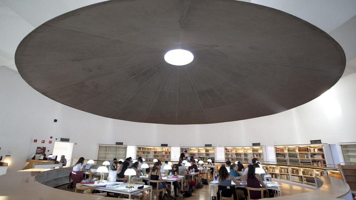 Imagen ilustrativa: un libro abierto sobre una mesa de madera junto a una ventana al atardecer, con estanterías desenfocadas al fondo.