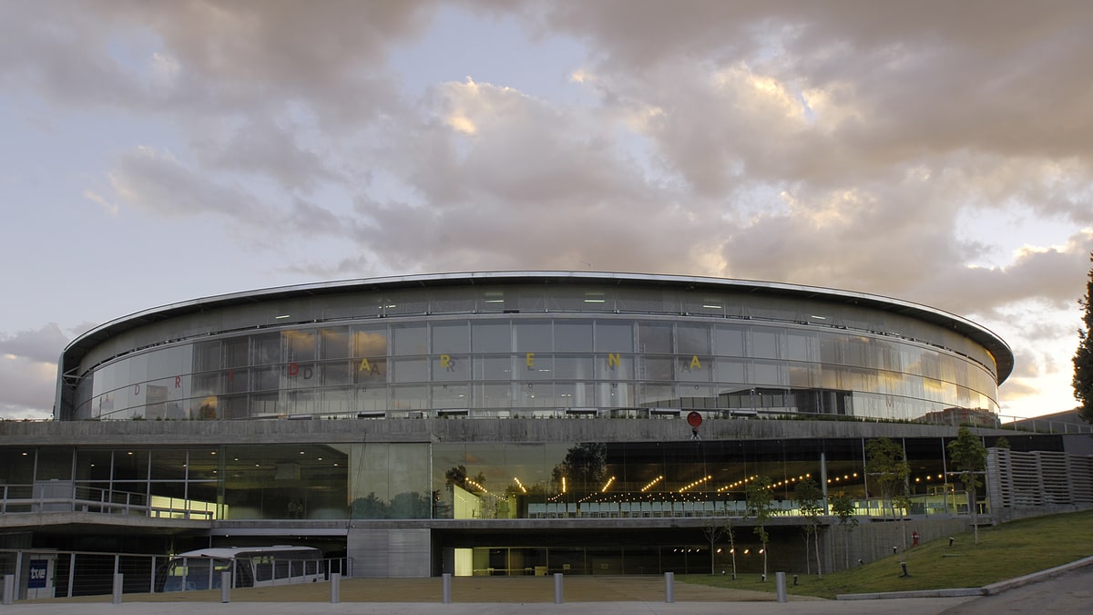 Fachada curva de cristal del Madrid Arena bajo un cielo nuboso al atardecer, sin público visible.