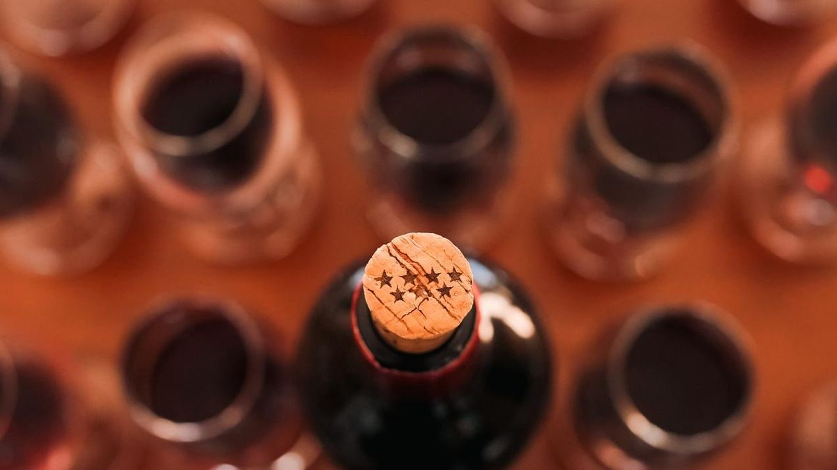Imagen ilustrativa: copa de vino tinto sobre una mesa de madera junto a una botella sin etiqueta en una sala de catas vacía