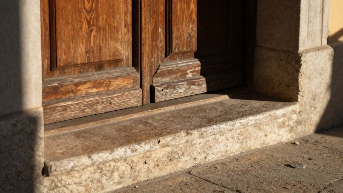 Imagen ilustrativa: primer plano de un umbral de madera envejecida y escalones de piedra al atardecer