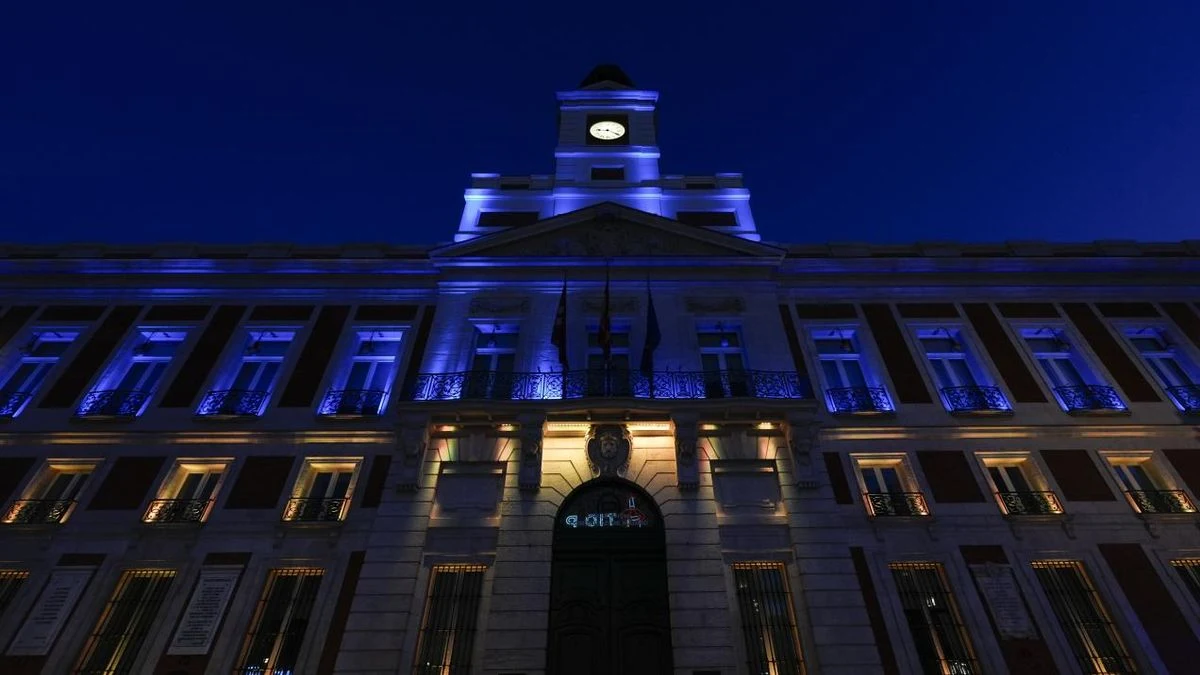 Imagen ilustrativa: fachada de un edificio institucional iluminada en azul y amarillo al atardecer, con sombras largas