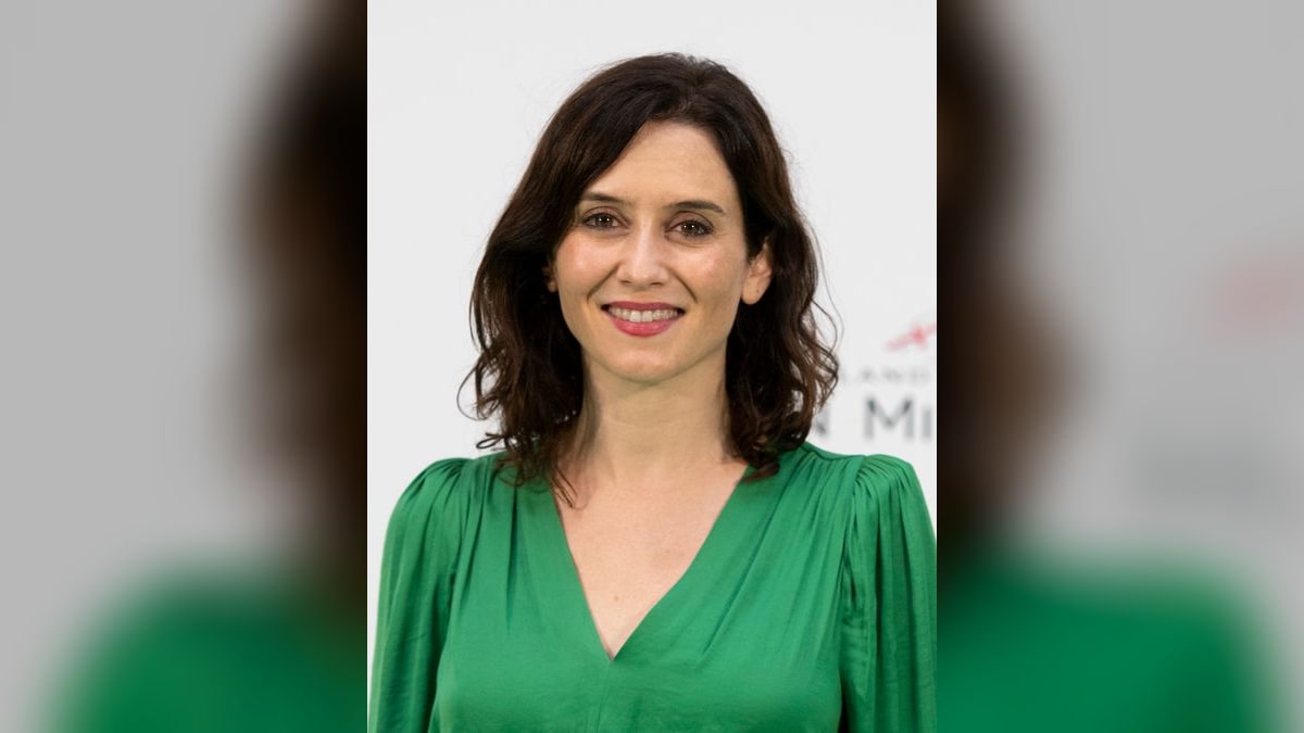 Isabel Díaz Ayuso sonriente con blusa verde frente a un fondo blanco de evento