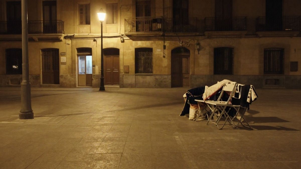 Imagen ilustrativa: plaza urbana nocturna con farolas encendidas y sillas plegables junto a una pared