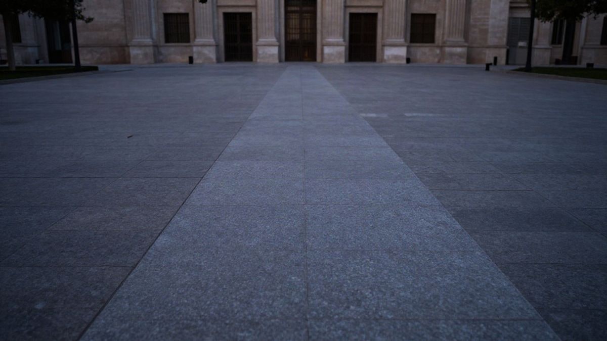 Imagen ilustrativa: una plaza empedrada vacía al atardecer, con un camino que converge hacia la fachada sobria de un edificio institucional