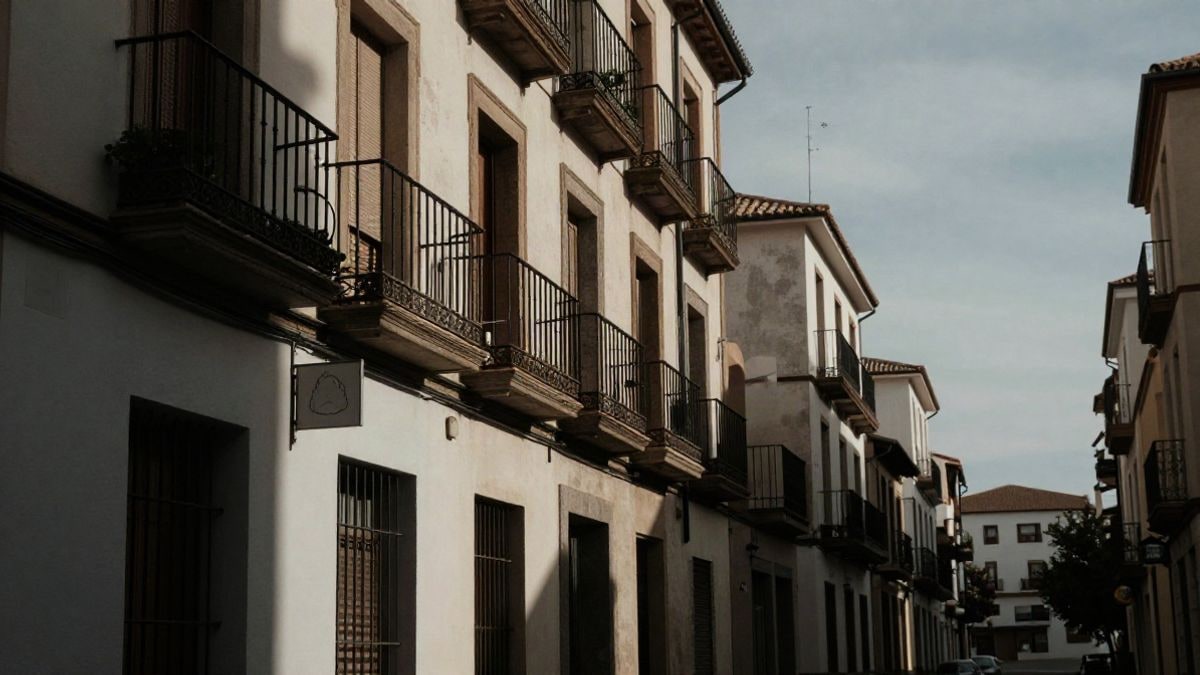 Imagen ilustrativa: calle residencial estrecha con balcones y un cartel en una fachada, iluminada por la tarde