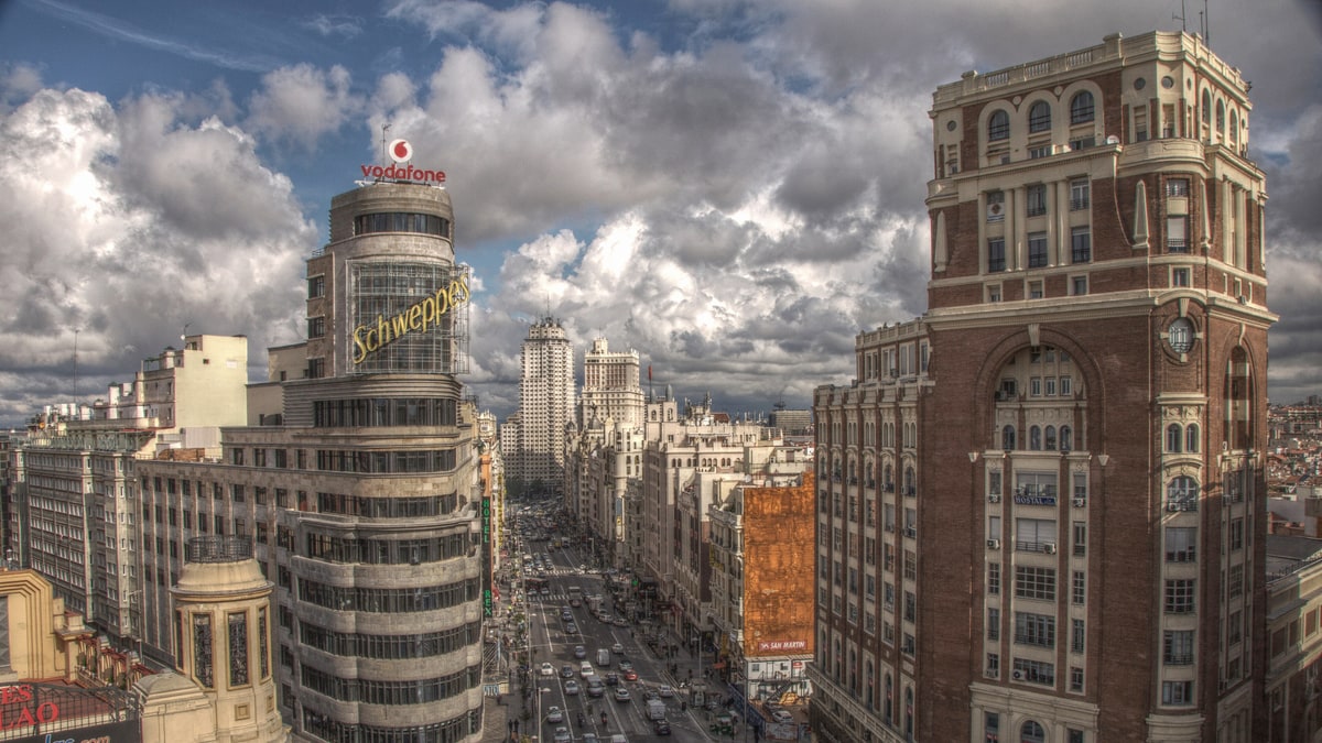 Vista aérea de la Gran Vía madrileña con tráfico, edificios históricos y cielo nublado dramático