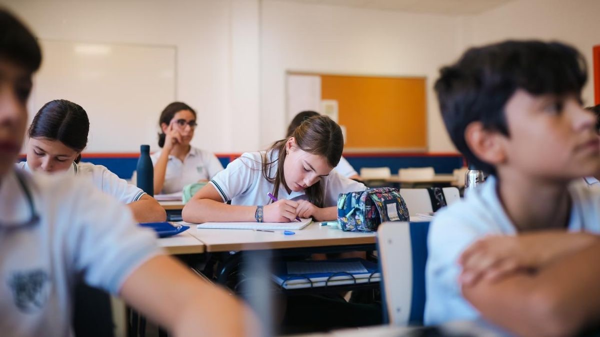 Imagen ilustrativa: un libro de inglés abierto y un lápiz sobre un pupitre de aula vacía con luz de ventana