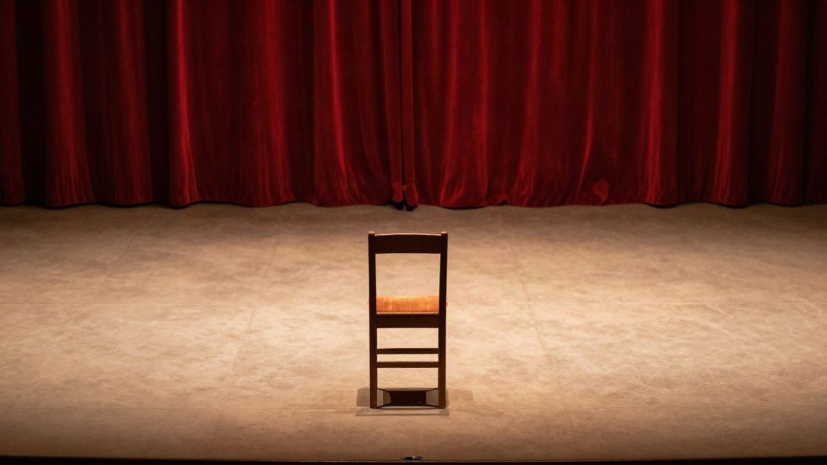 Imagen ilustrativa: una silla de madera sola en un escenario vacío de teatro, iluminada por una luz cálida lateral