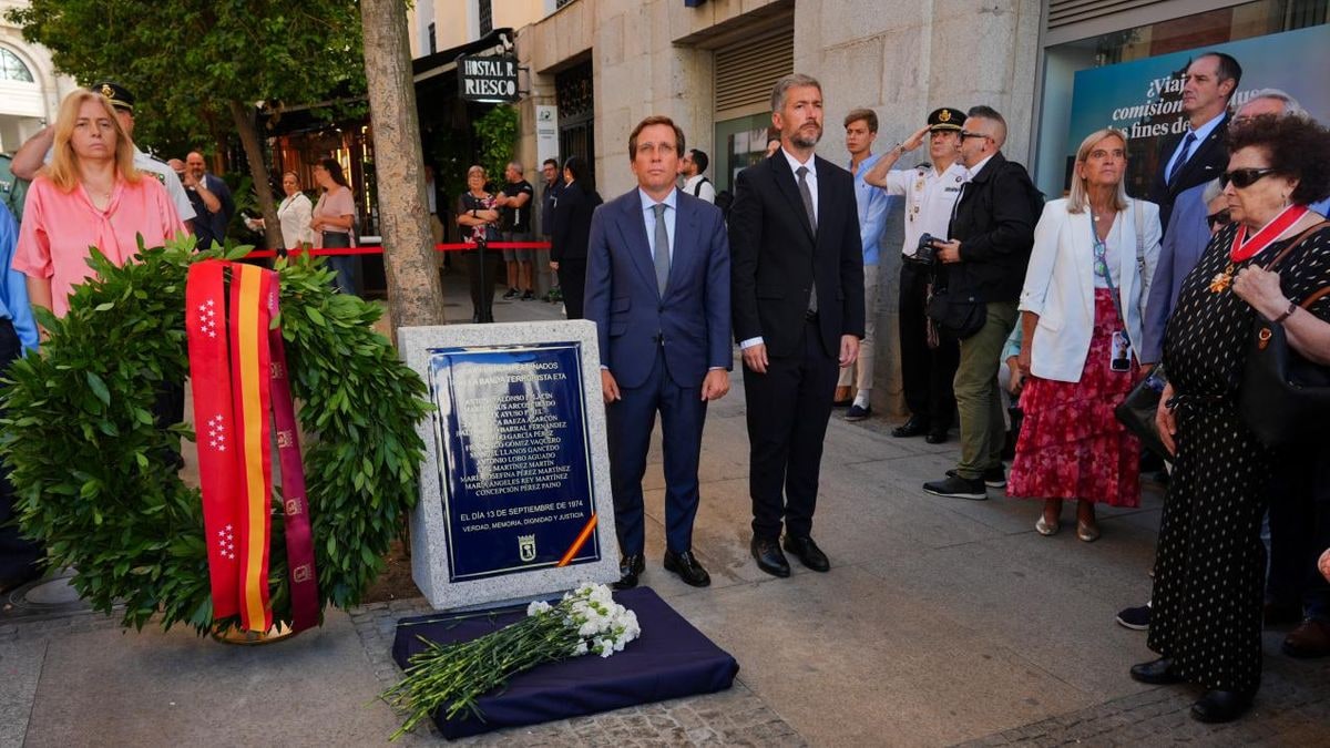 Imagen ilustrativa: placa conmemorativa en una pared de piedra con una vela y flores blancas en una calle urbana