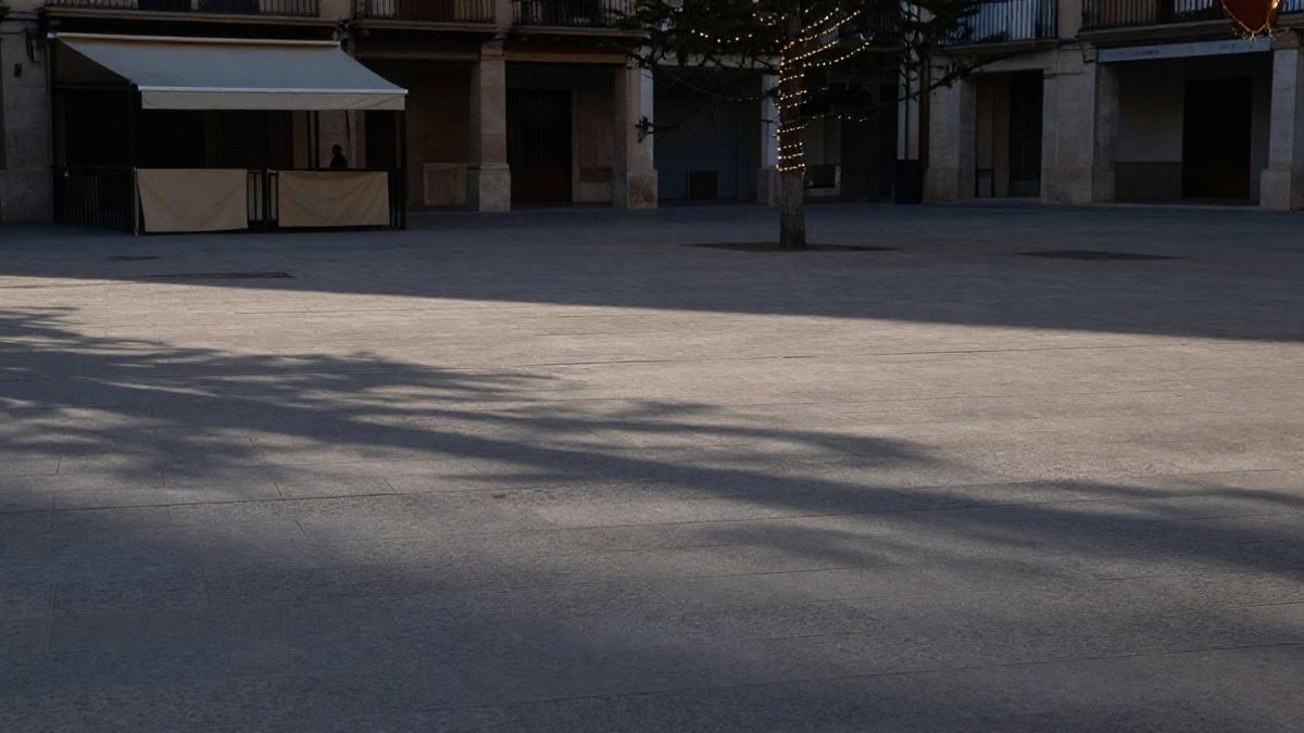 Imagen ilustrativa: una plaza urbana vacía al atardecer, con un toldo plegado y un abeto sin decorar al fondo