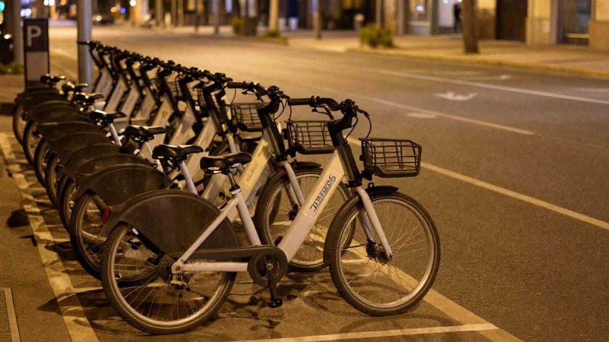 Imagen ilustrativa: bicicletas eléctricas compartidas aparcadas en una zona delimitada con marcas en el suelo bajo luz artificial nocturna