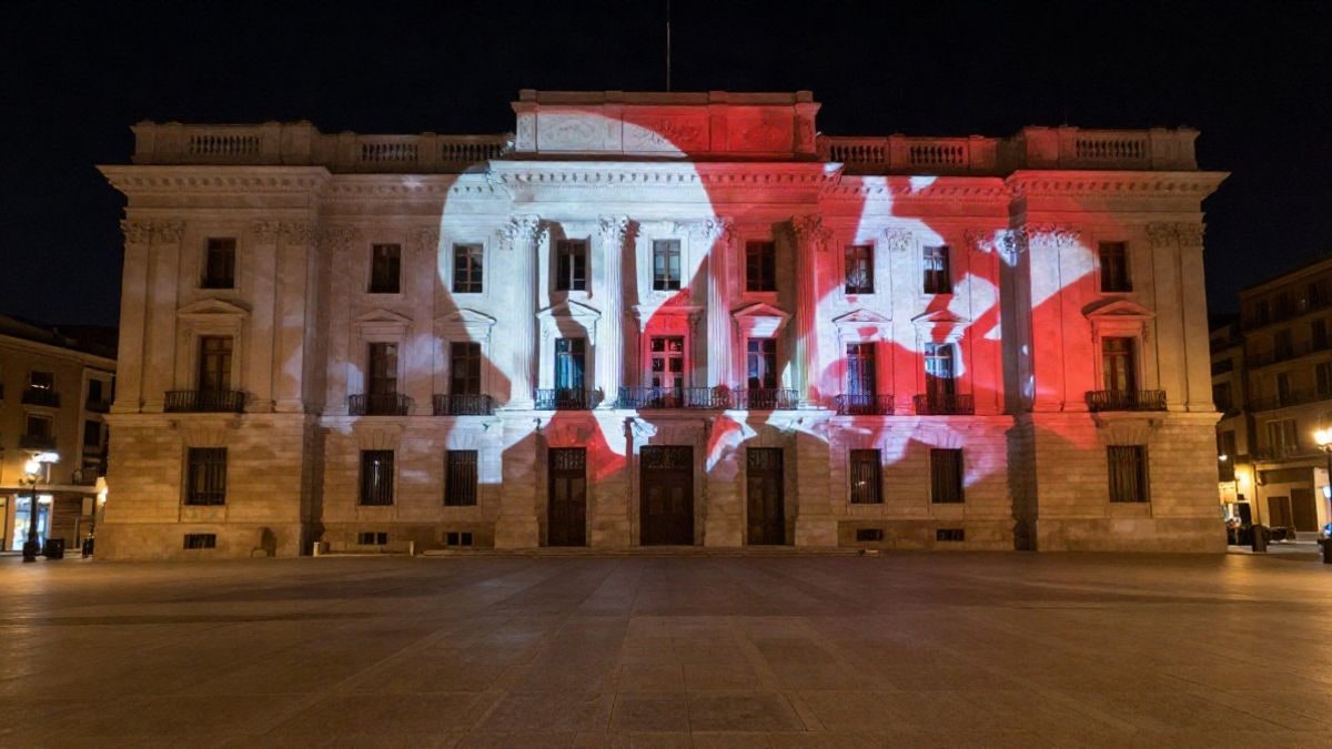 Imagen ilustrativa: fachada de un edificio señorial iluminada por una proyección de luz nocturna en una plaza