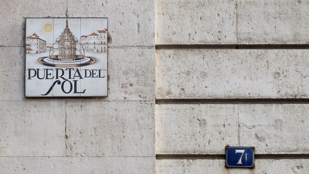 Azulejo con la fuente y el nombre Puerta del Sol junto al número 7 en una fachada de piedra clara.