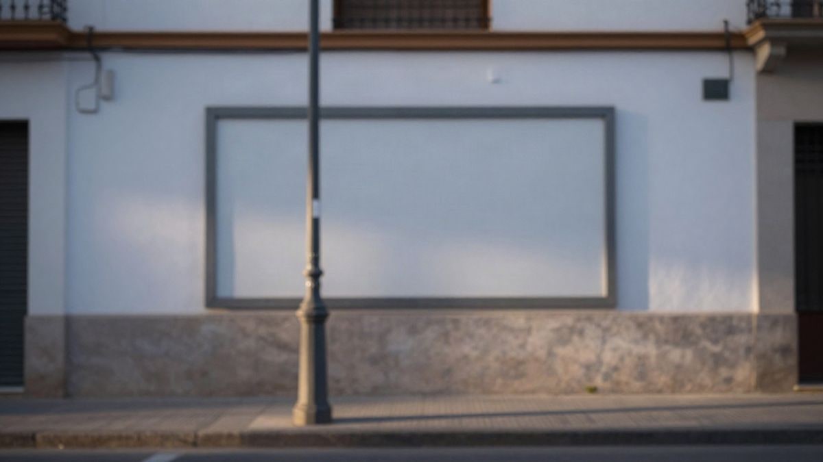 Imagen ilustrativa: fachada blanca de un edificio urbano al atardecer, con un panel rectangular vacío y una farola en primer plano