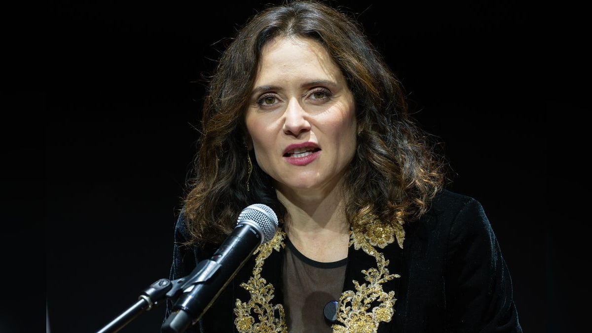 Isabel Díaz Ayuso habla ante un micrófono sobre fondo negro, vistiendo chaqueta de terciopelo bordada