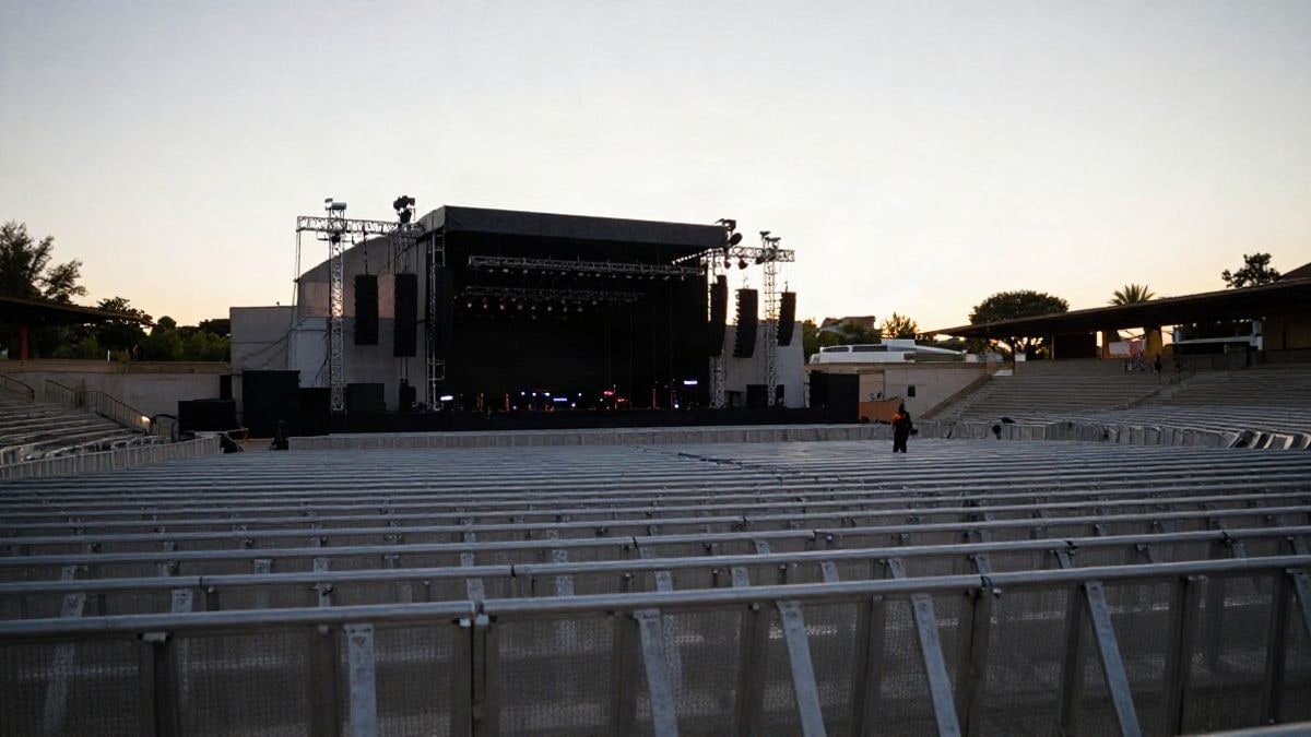 Imagen ilustrativa: un recinto de conciertos al aire libre al atardecer con el escenario al fondo y vallas metálicas en primer plano