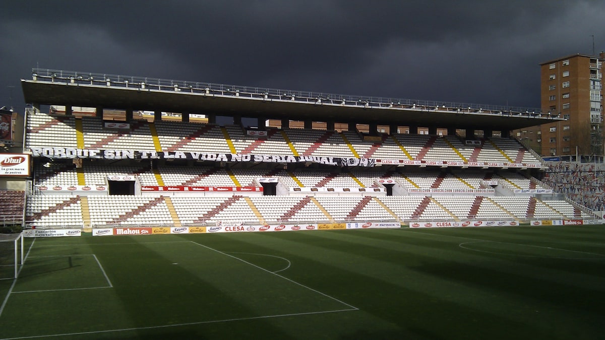 Estadio de Vallecas bajo cielo oscuro, con pancarta en la grada y el campo vacío de jugadores