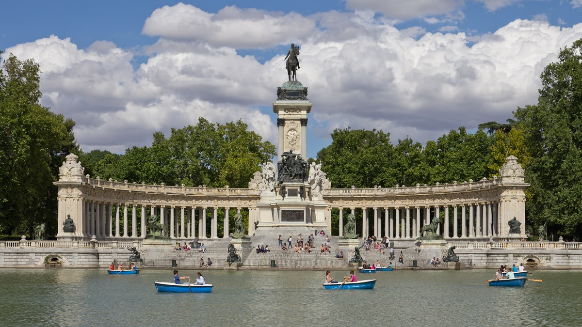 Monumento a Alfonso XII en el Estanque del Retiro, con barcas de remos y nubes al fondo.