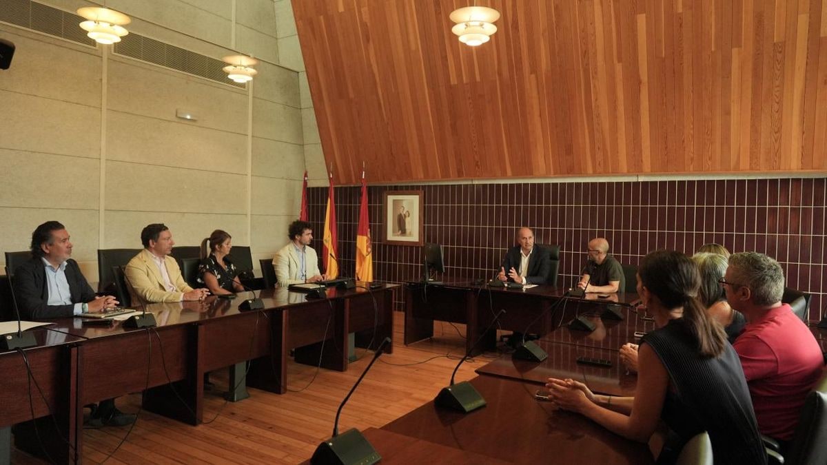 Imagen ilustrativa: un teléfono móvil sobre una mesa de madera con un edificio consistorial desenfocado al fondo