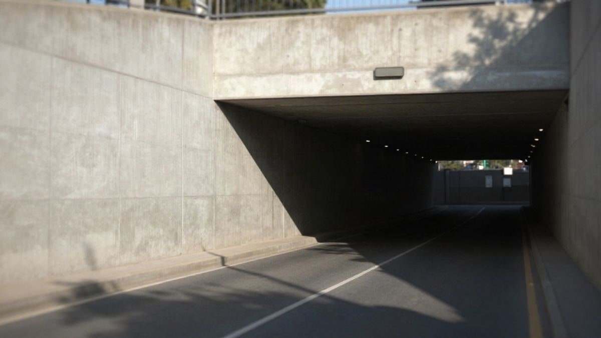 Imagen ilustrativa: entrada de un túnel urbano moderno con muros de hormigón y una calzada vacía al atardecer