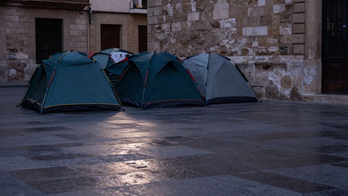 Imagen ilustrativa: tiendas de campaña plegadas junto a un muro de piedra en una plaza vacía al amanecer