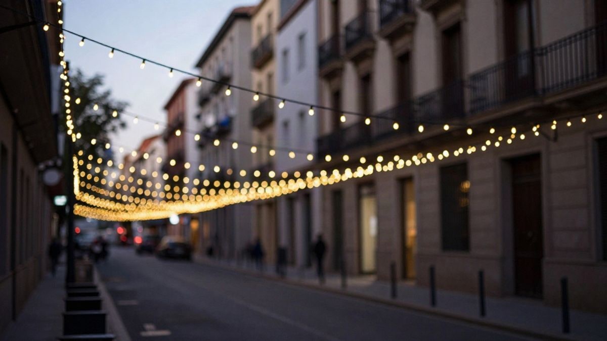 Imagen ilustrativa: una hilera de luces blancas cálidas cruza una calle al atardecer, con fachadas desenfocadas al fondo