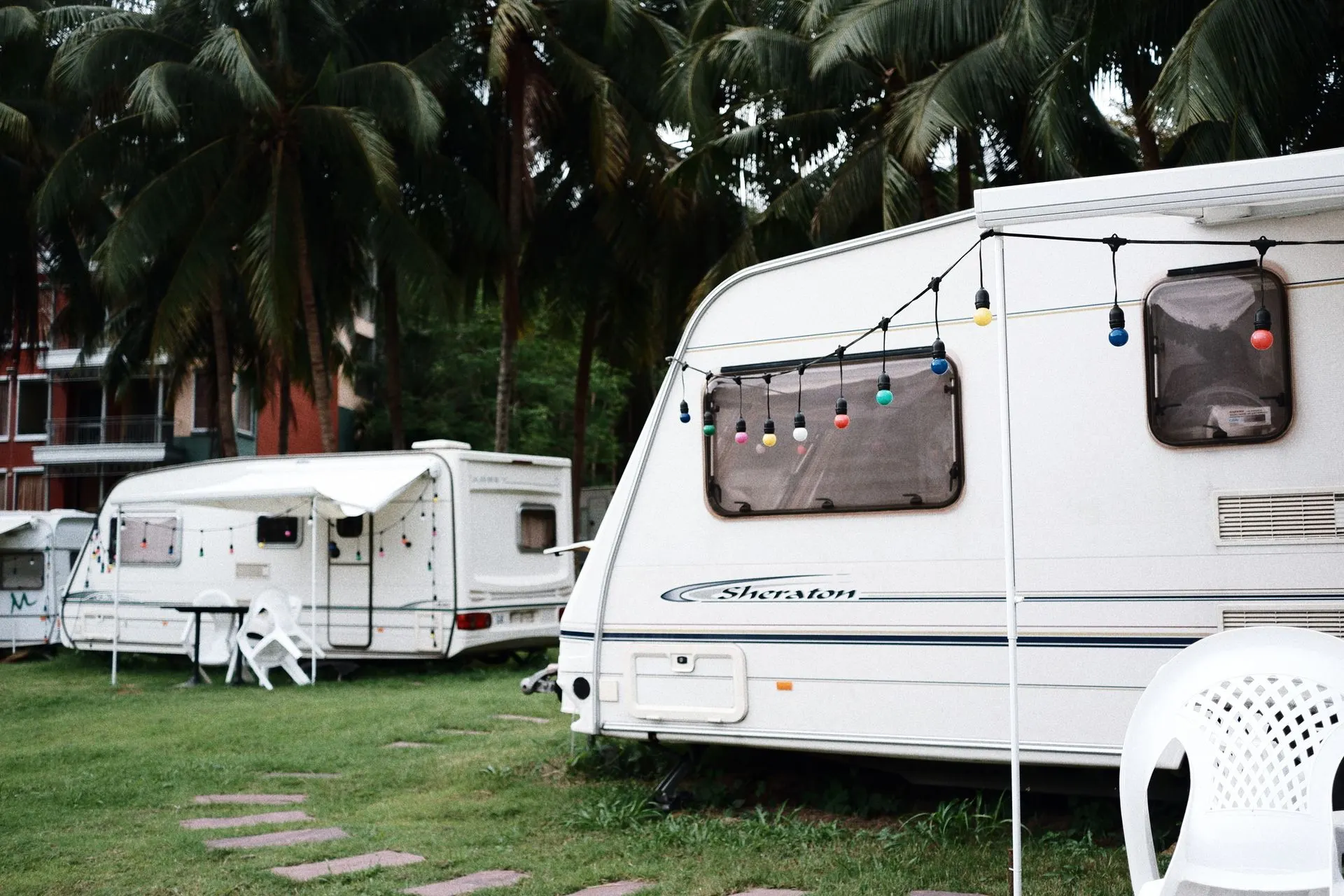 Relajante sitio de camping con caravanas bajo palmeras, con asientos al aire libre y luces festivas