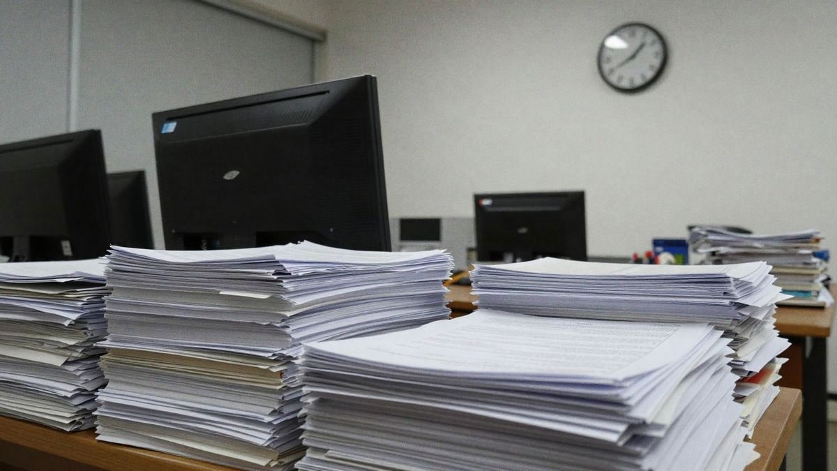 Oficina ocupada con papeles, computadora y reloj marcando horas tardías, reflejando un ambiente de trabajo enfocado.