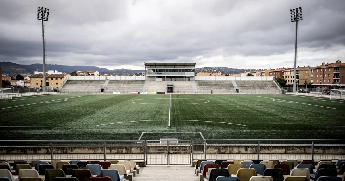 Estadio vacío con césped artificial representando el fútbol modesto español.
